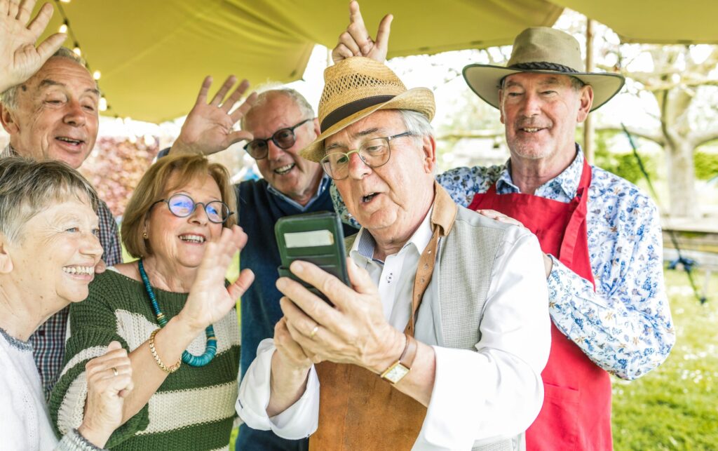A group of retired friends enjoys using technology during an outdoor barbecue.