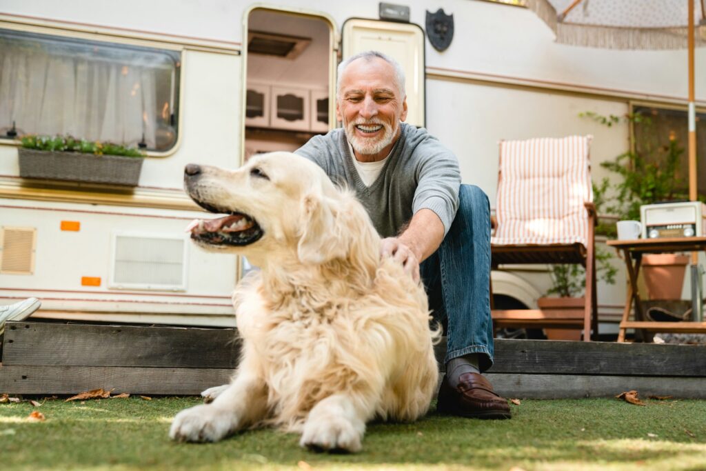 Active old senior man adventurer explorer playing with dog near trailer.